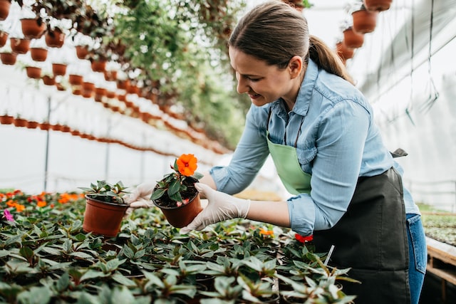 Happy and positive young adult woman working in greenhouse and enjoying in beautiful flowers