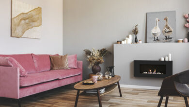 Paintings on the walls of grey living room interior with pink couch and bio fireplace